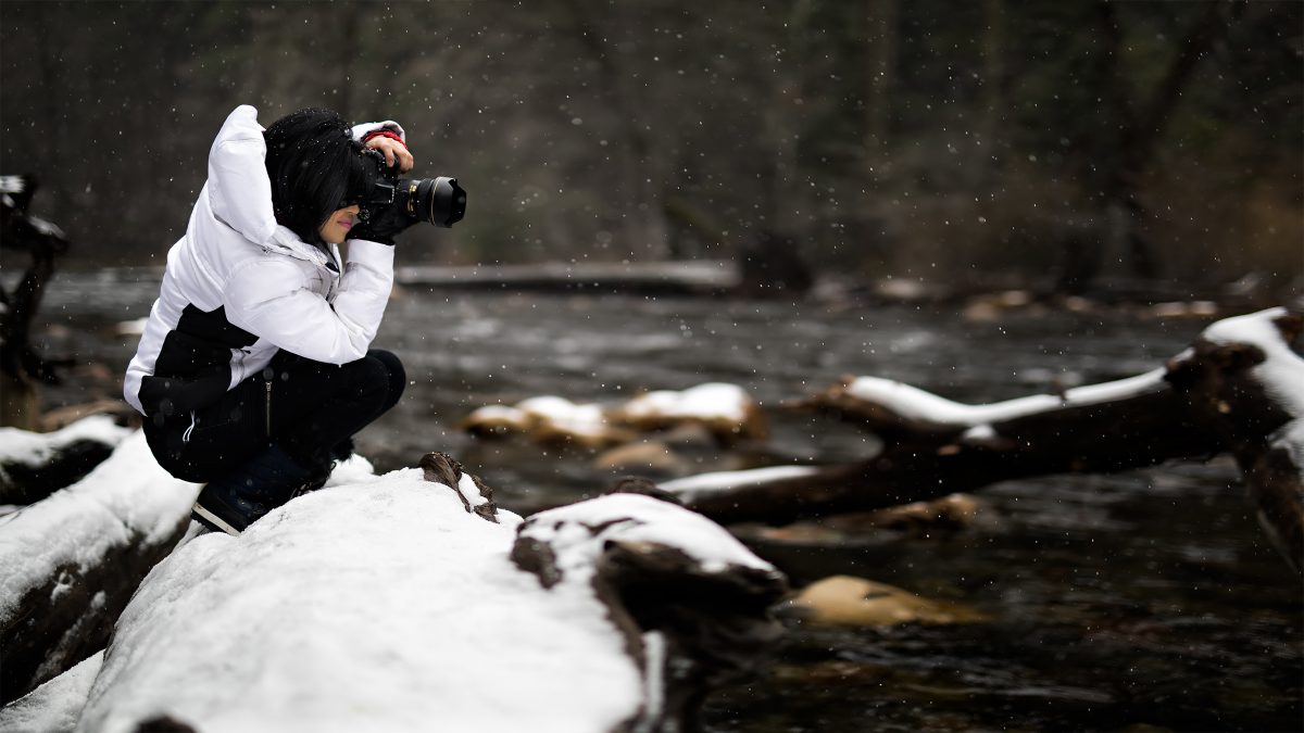 Female photographer takes pictures with camera by the river during winter